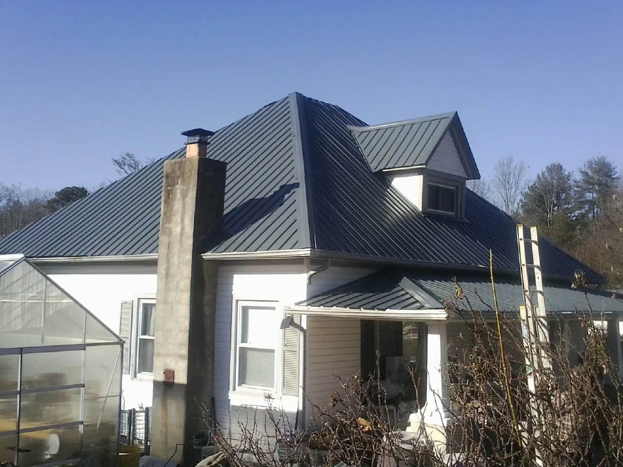 Dark blue standing seam metal roof on a white farmhouse with dormer — Slate & Tile Roof Repair by Roofing Brothers in Nesmith