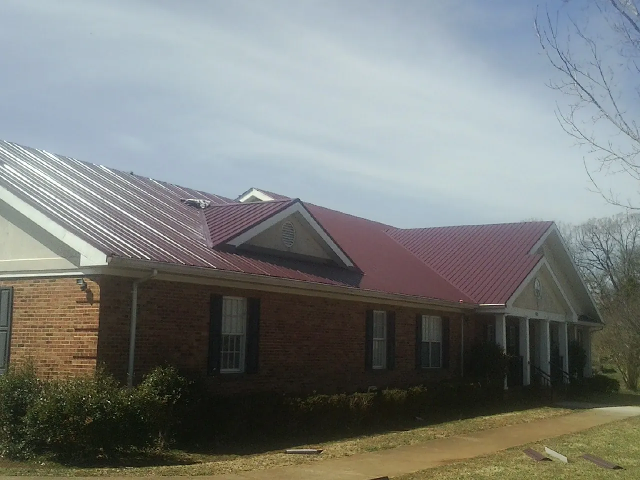 Red metal roof with gabled entries on a long brick building, from a Hail Damage Roof Repair job in Nesmith