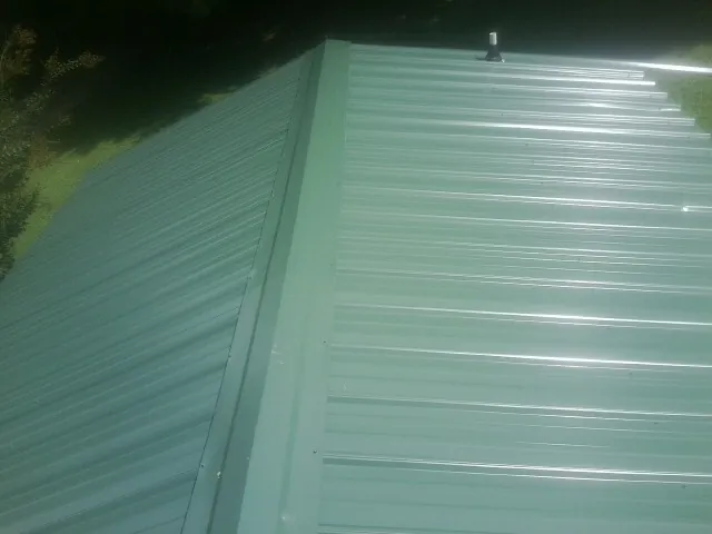 New green metal panels meeting at the ridge of a roof — Flat Roof Repair work by our crew in Nesmith