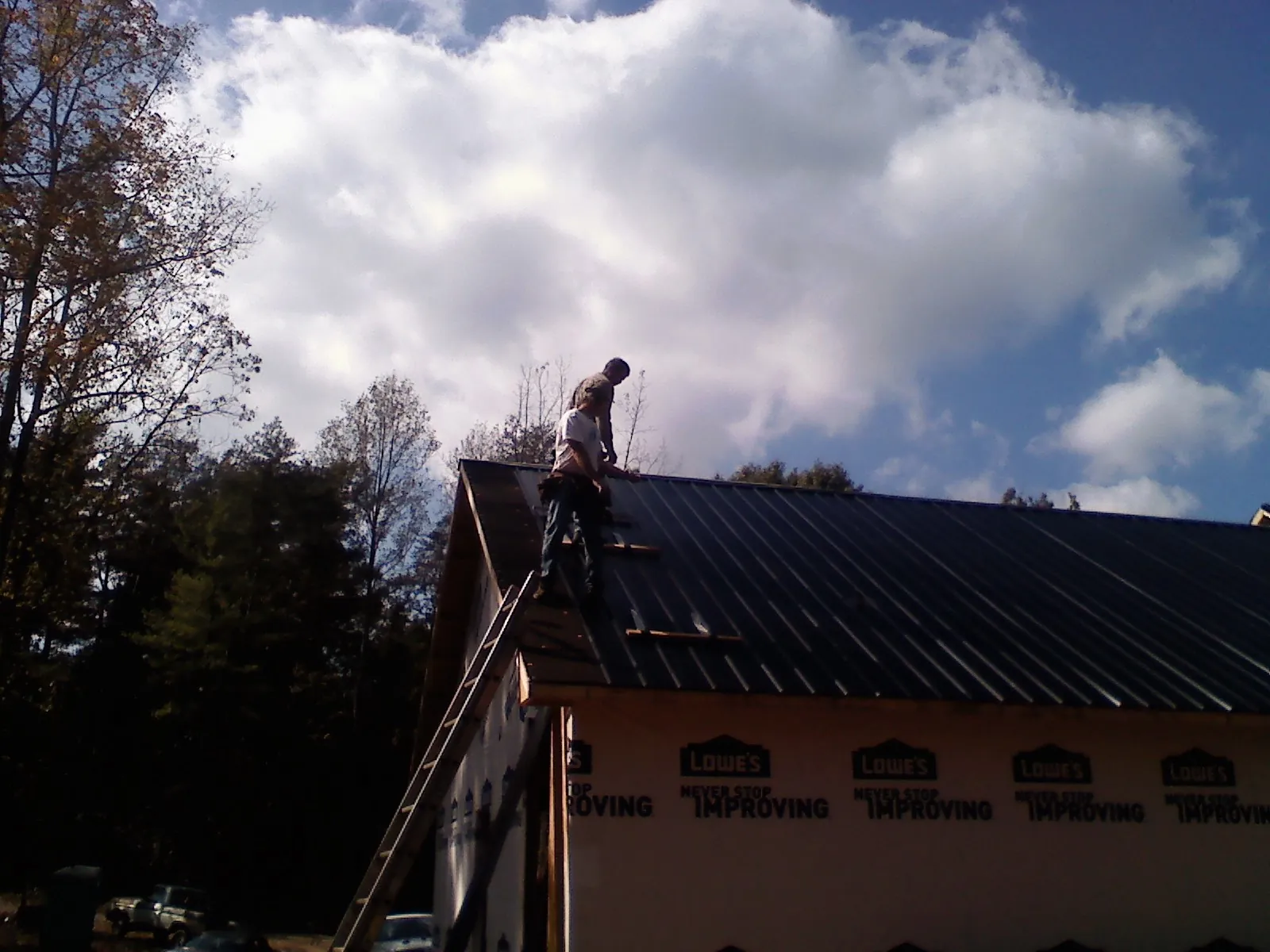 Roofer fastening dark metal panels high against a cloudy sky, from a Roof Inspection job in Nesmith